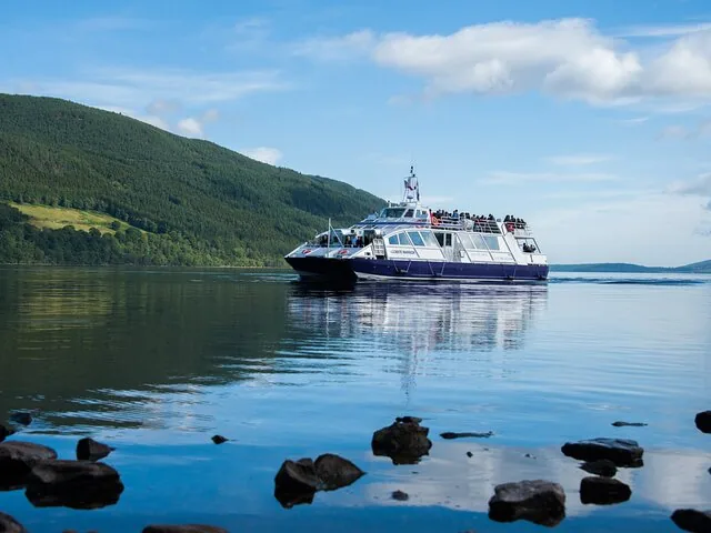 A passenger ferry cruising on a calm loch under a partly cloudy sky.