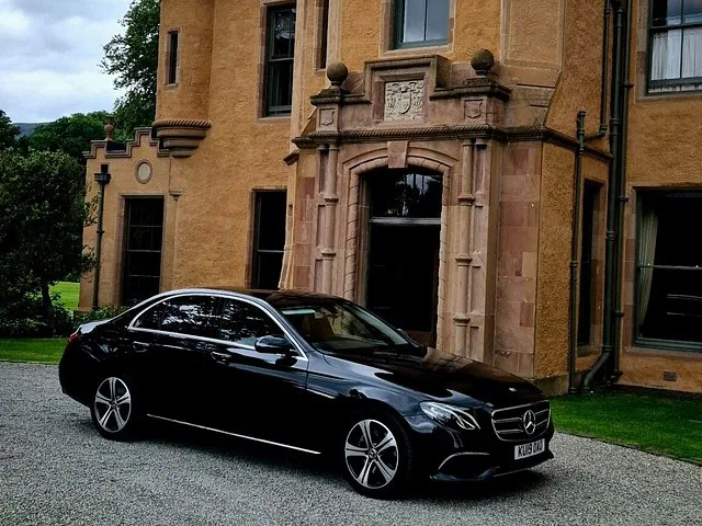 A black luxury car parked in front of a grand, historic stone building.