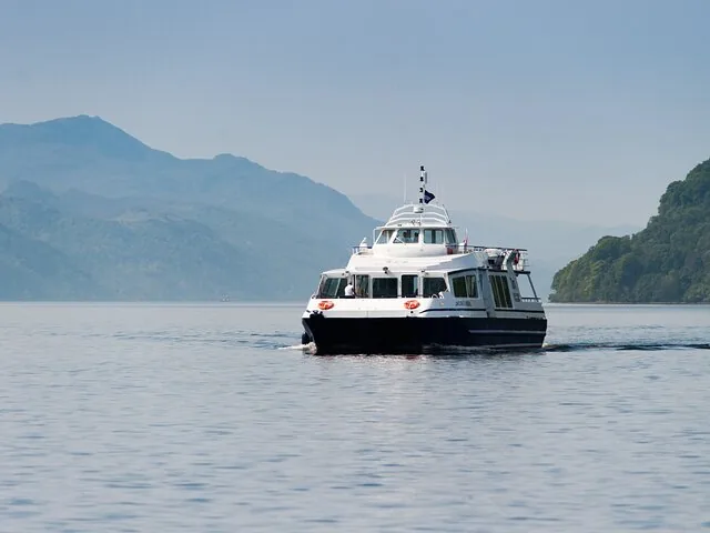 A passenger ferry approaches on a serene loch surrounded by rolling hills.