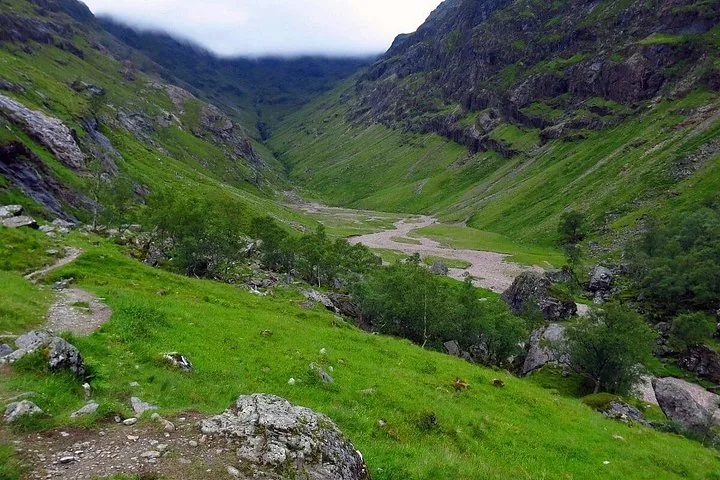 Ruins of a stone castle standing on a grassy hill beside a loch.