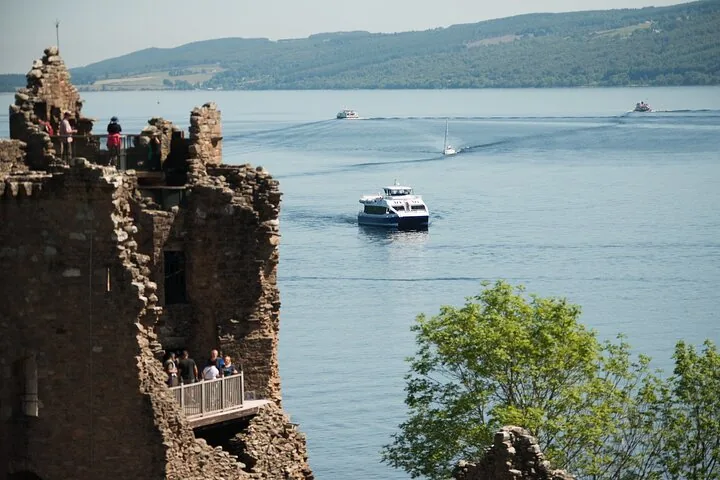 A boat sails past stone castle ruins on a sunny day.