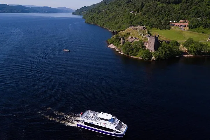 Aerial view of a boat cruising past historic castle ruins by a loch.