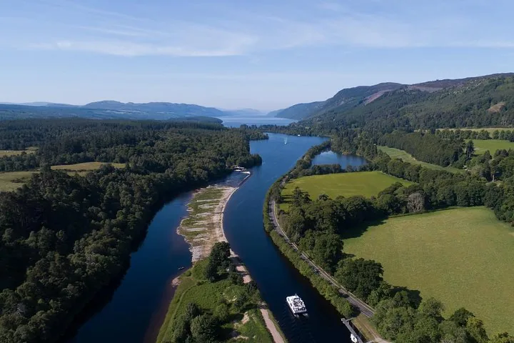 Aerial view of a boat navigating a scenic river surrounded by forests.
