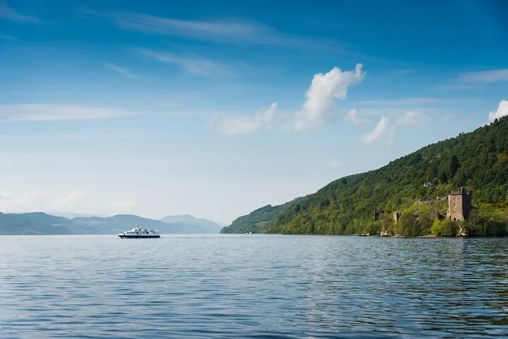 A boat sails on a calm loch near coastal castle ruins.