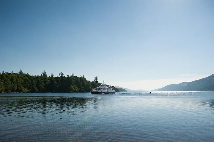 A passenger boat glides over a smooth loch framed by green hills.