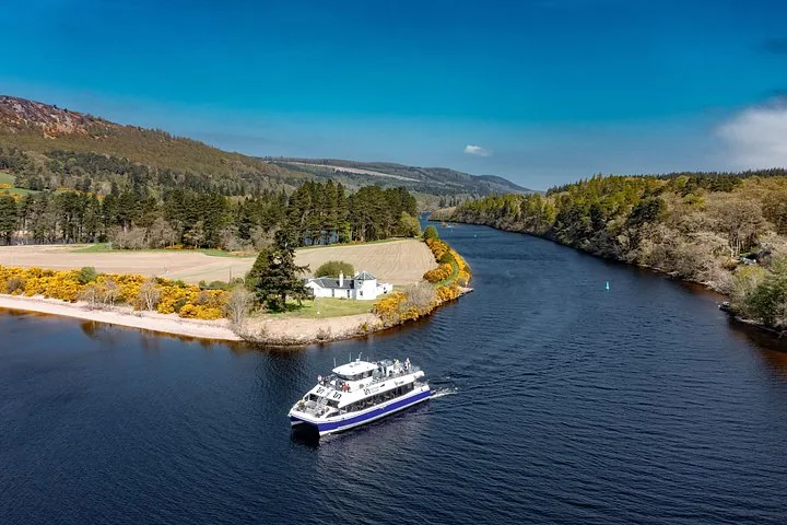 A passenger ferry navigating a waterway bordered by trees and a house.